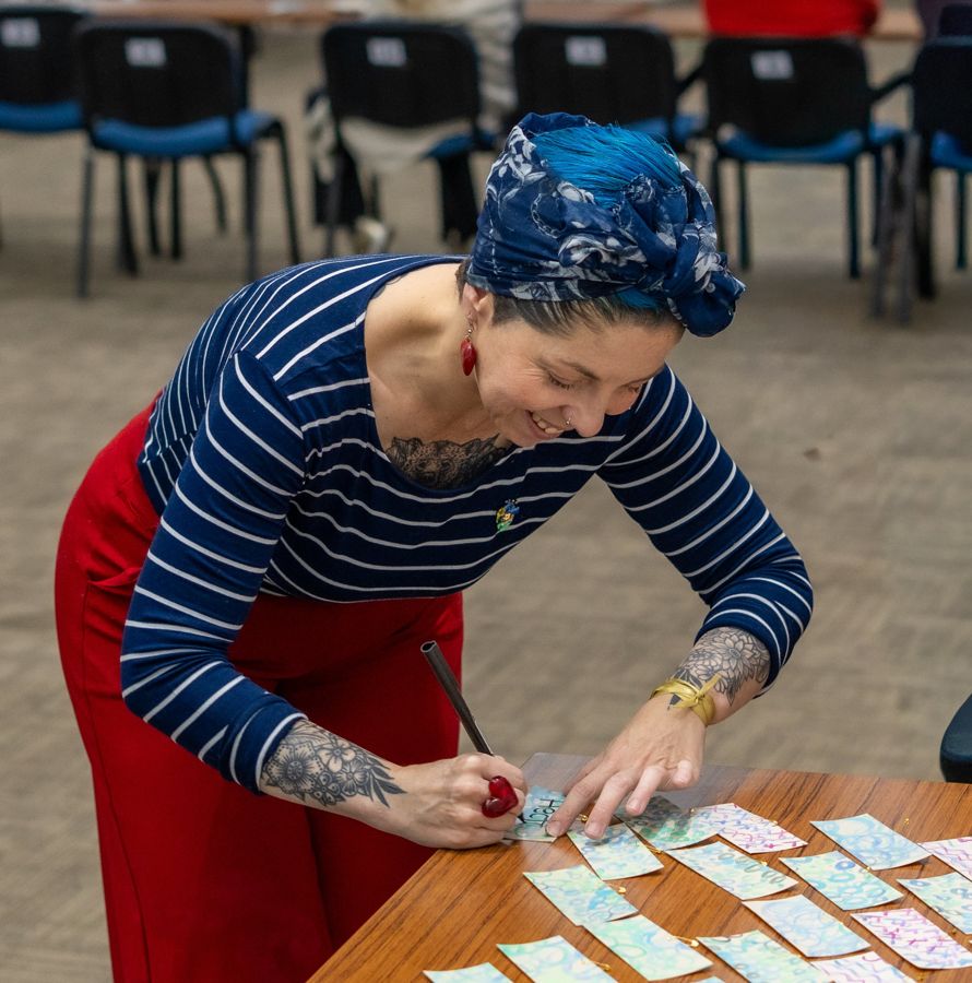 Nathalia sonriendo mientras escribe sobre tarjetas pintadas con acuarela