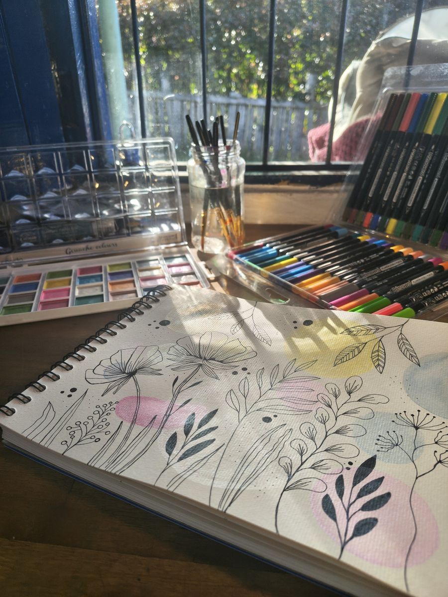 Cuaderno con flores dibujadas en tinta y acuarela junto a una ventana con luz de la mañana