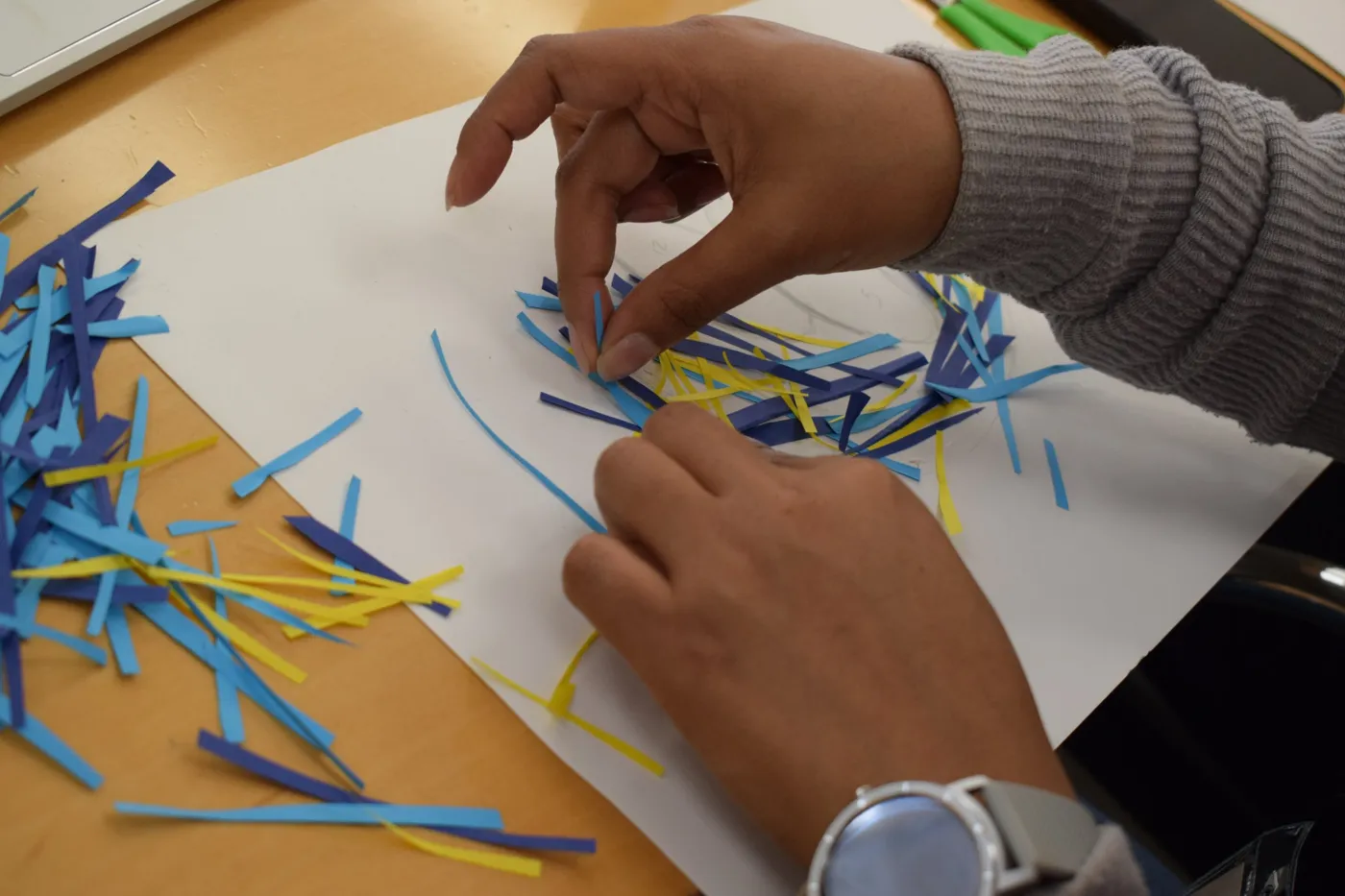 Manos que arman un collage con tiras de papel azul y amarillo