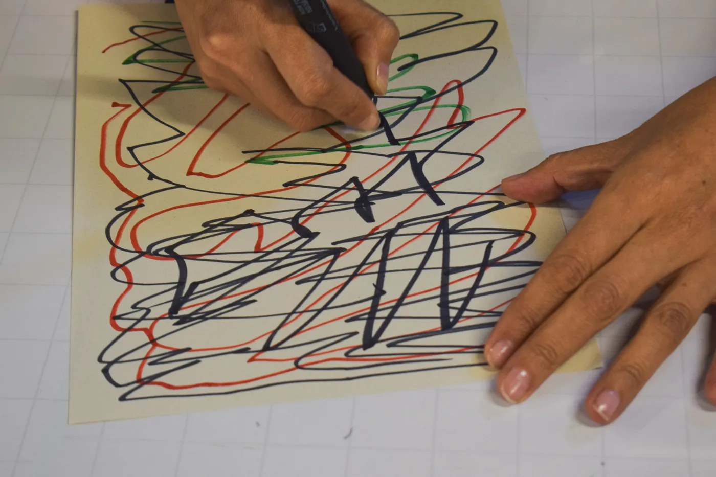 Una mano traza garabatos con marcadores negro, rojo y verde
