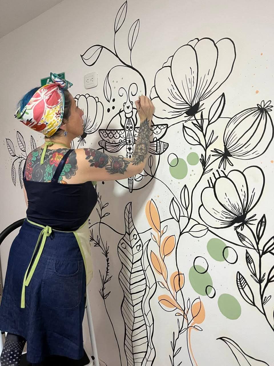 Nathalia pintando un mural de flores y hojas en tinta negra
