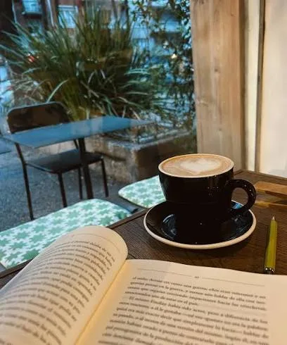Un libro abierto junto a una taza de café, en una mesa junto a la ventana